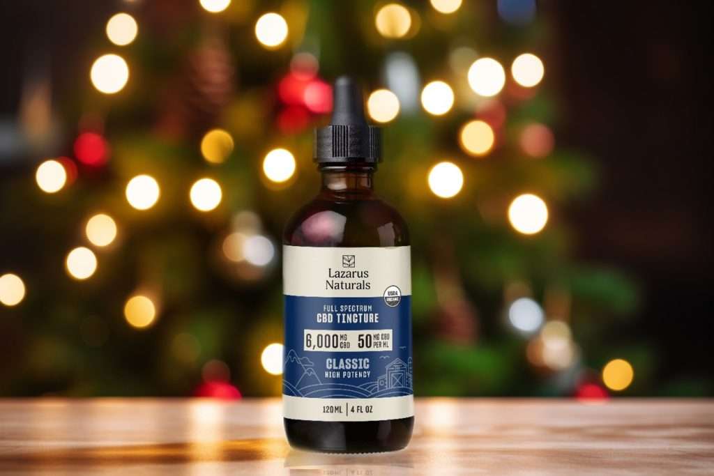 A bottle of Lazarus Naturals Full Spectrum CBD Tincture against a blurred background of festive Christmas tree lights.